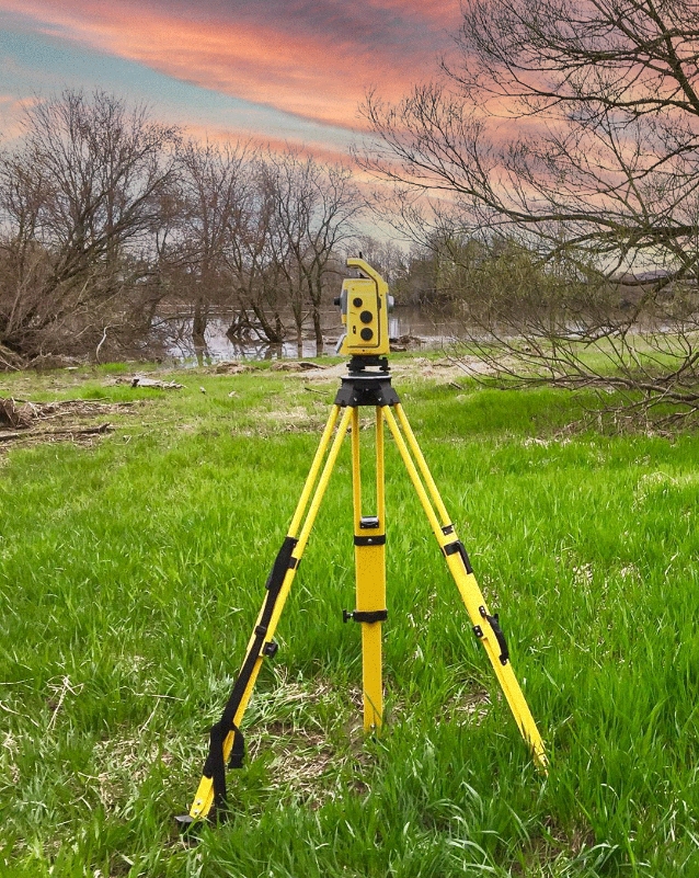 Théodolite jaune sur pied dans un champ verdoyant.